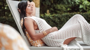 Una persona recostada en una silla de descanso blanca con funda estampada, rodeada de exuberante follaje.