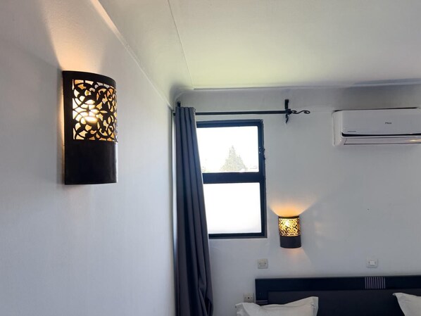 A hotel room with a bed, a window with curtains, a wall-mounted air conditioner, and a decorative wall light. - Hotel Islane City Center (Marrakech)