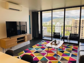 Ein modernes Wohnzimmer mit großem Fernseher, einem Essbereich und einem Balkon mit Blick auf die Stadt.