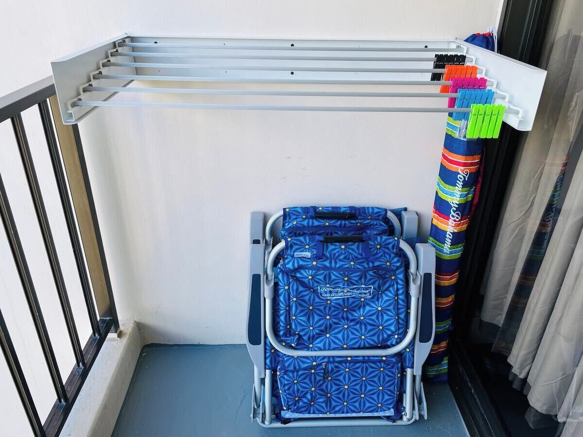 A balcony with a metal drying rack, a suitcase, and colorful curtains.