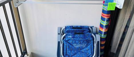 A balcony with a metal drying rack, a suitcase, and colorful curtains.