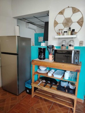 A compact kitchen with a stainless steel refrigerator, a microwave, and a wooden shelf holding kitchenware. - TROPIAL PARADISE ROOM H3 (La Libertad)