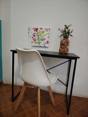 A white chair, a desk, a vase with flowers, and a wall with a floral painting. - TROPIAL PARADISE ROOM H3 (La Libertad)