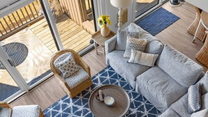 A modern living room with a sectional sofa, a coffee table, a patterned rug, and wicker furniture. - Aerie at Gentle Winds (Glen Arbor)