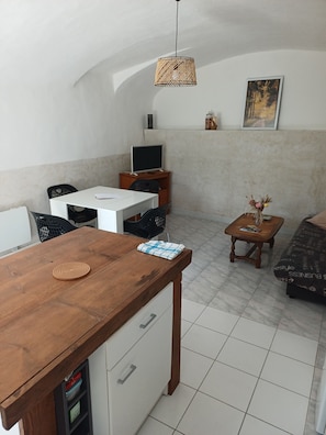 Un coin repas comprenant une table en bois, des chaises, un téléviseur et une petite table d’appoint sur laquelle est posé un vase.