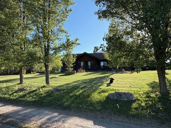 A log cabin with a porch, surrounded by trees and a grassy yard. - My Dad's Log Cabin (Fairlawn)