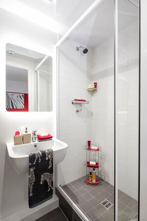 Un baño moderno con lavamanos, espejo y ducha blancos.