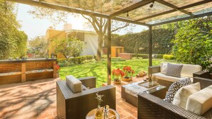 A covered outdoor seating area with wicker furniture, a brick wall, and a view of a well-maintained garden. - Casa Azteca (Mexico City)
