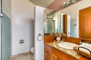 Un baño con tocador de madera, un lavamanos, un espejo, toallero y un inodoro.