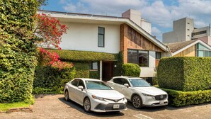 A modern two-story house with a paved driveway and two parked cars. - Casa Azteca (Mexico City)