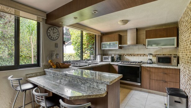 A modern kitchen with a large island, bar stools, a microwave, stove, and a clock on the wall. - Casa Azteca (Mexico City)