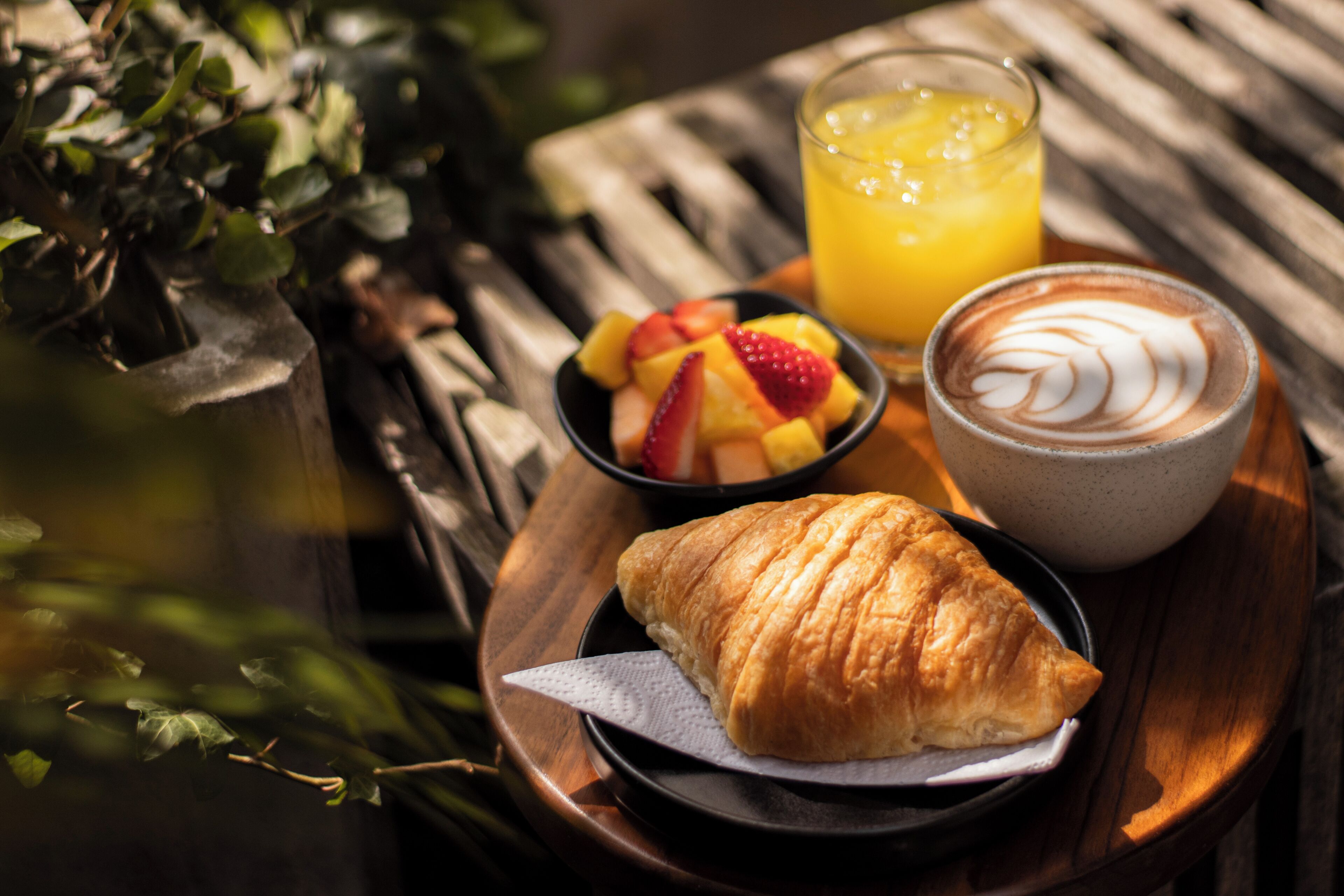 Une table en bois avec un croissant, des fruits et un verre de jus d’orange.