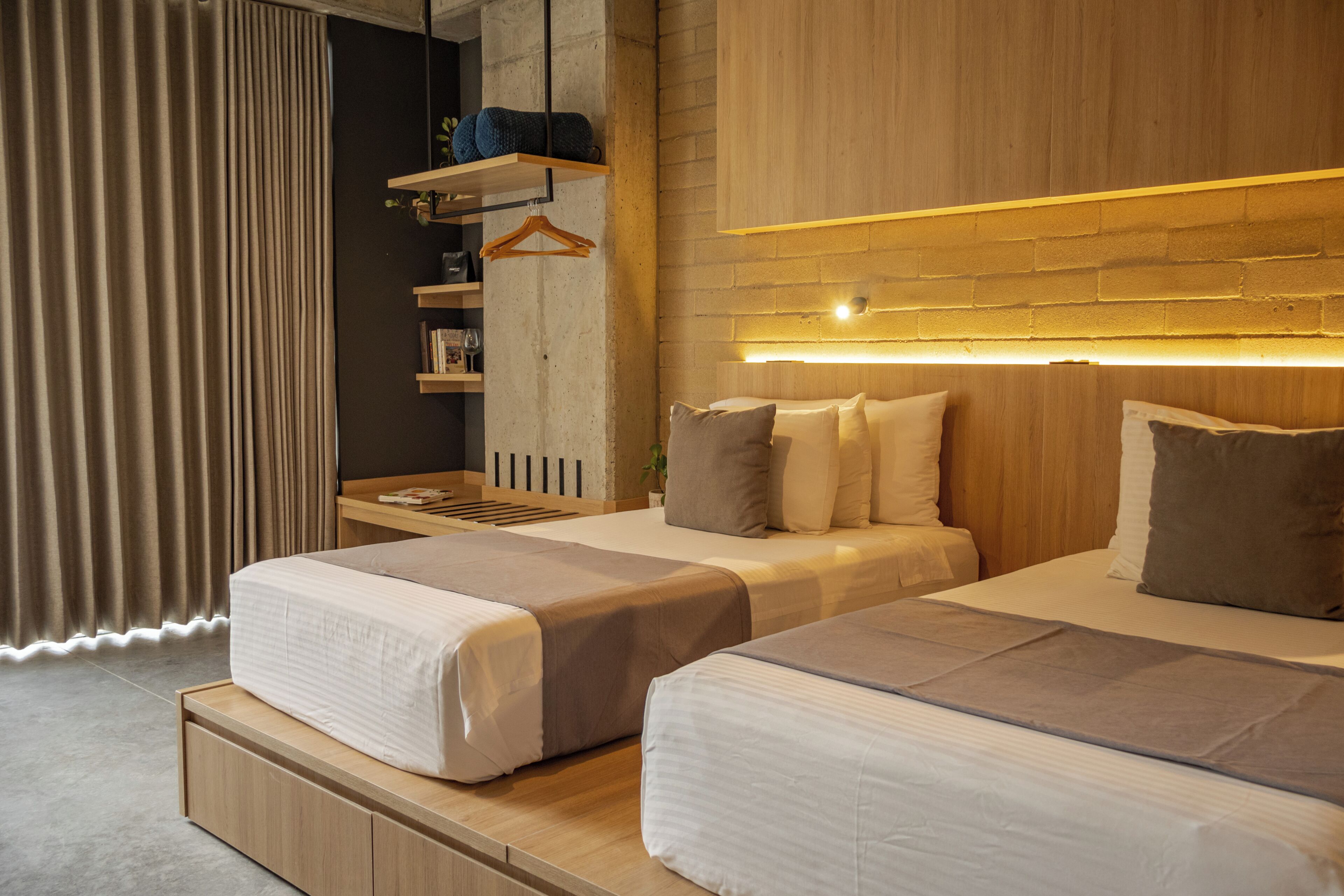 A modern hotel room with two beds, a wooden headboard, a bedside table, and a hanging plant.
