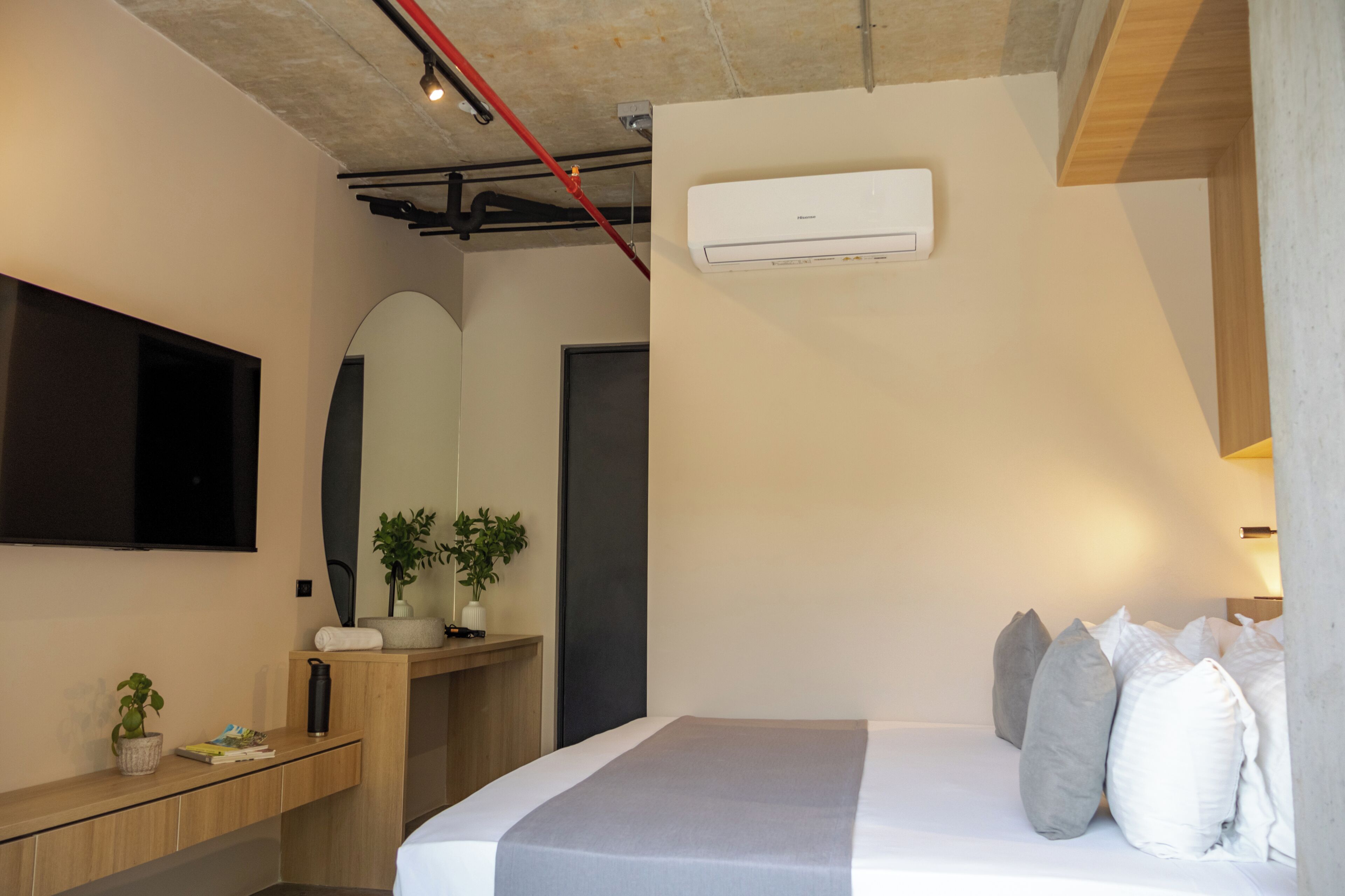 Un dormitorio moderno con una cama, almohadas, una mesita de noche con una planta, un espejo y un equipo de aire acondicionado.