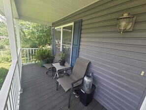 A covered porch with a table, chairs, a potted plant, and a water dispenser.