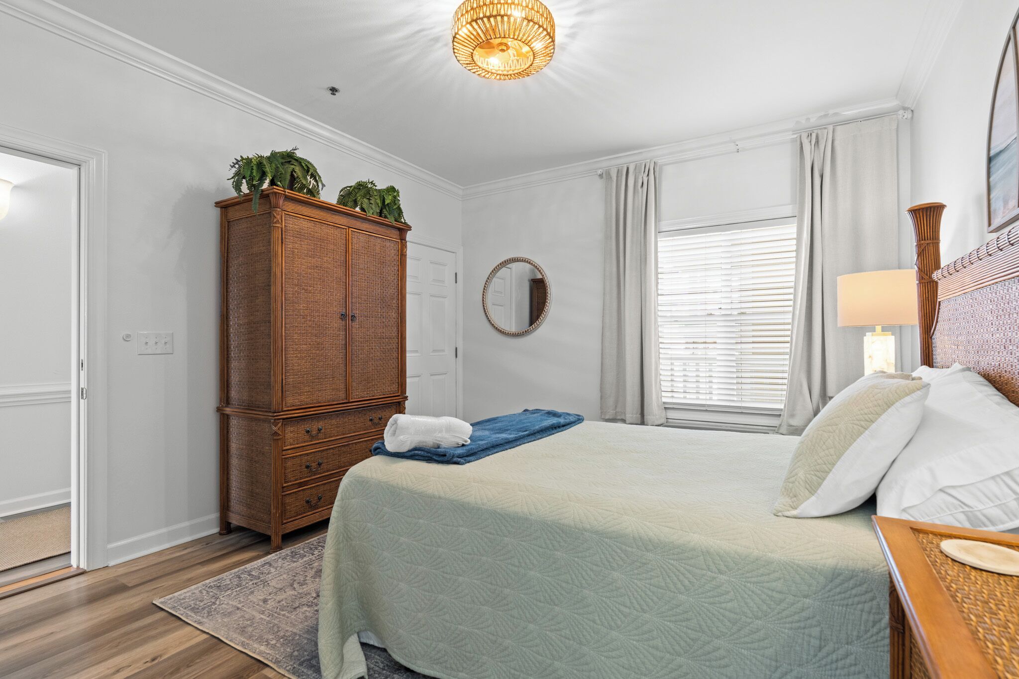 A bedroom with a bed, a wooden wardrobe, a mirror, and a window with curtains.