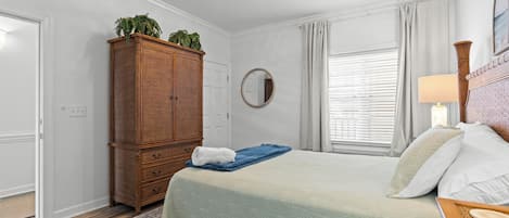 A bedroom with a bed, a wooden wardrobe, a mirror, and a window with curtains.