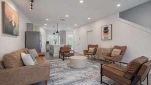 Una sala moderna con sofá, sillas, una mesa de centro y una cocina al fondo.