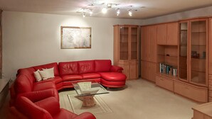 Un salon avec un canapé rouge, une table basse en verre, un meuble en bois doté de portes en verre et un tableau accroché au mur.
