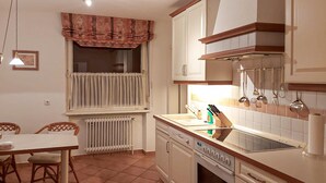 Une cuisine équipée d’une table à manger, de chaises, d’une fenêtre avec des rideaux, d’un radiateur, d’une cuisinière et d’un évier.
