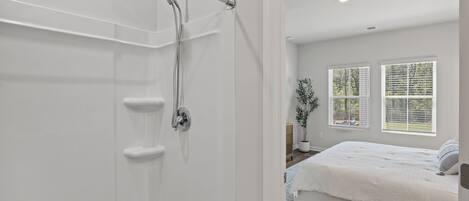 Een badkamer met een douche, toilet en wastafel. Er is een bed met een witte dekbedovertrek en een blauw vloerkleed.