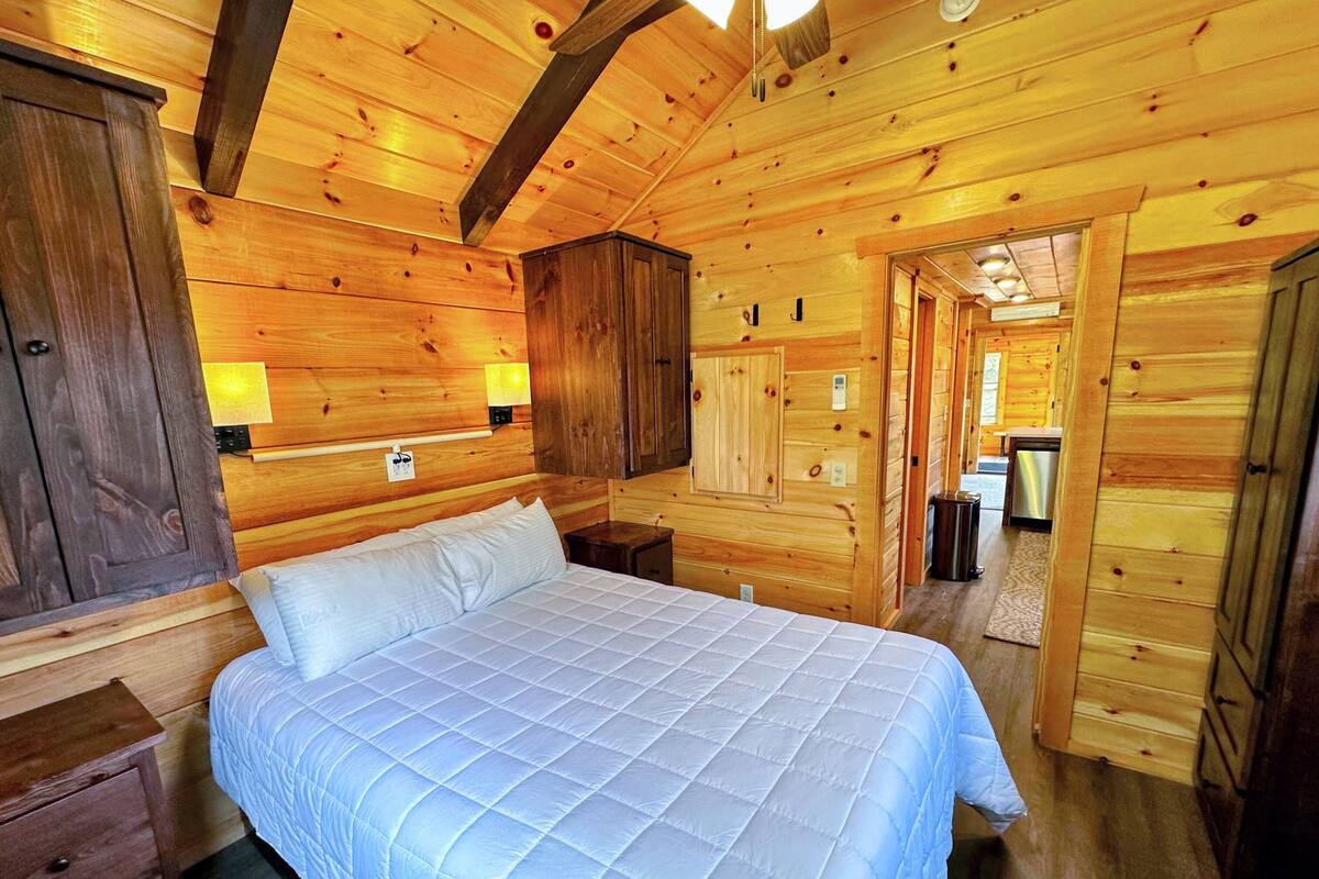 L’intérieur d’une cabane en bois, avec un lit, des murs en bois et une petite cuisine.