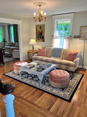 A living room with a sofa, ottomans, a coffee table, a lamp, and a painting on the wall.