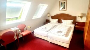 Una habitación con cama, dos ventanas, un escritorio y una silla.