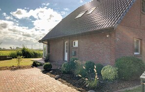 Ein Ziegelhaus mit einem Ziegeldach, einer Haustür und einem kleinen Garten mit Sträuchern und einer gepflasterten Auffahrt.