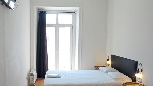 A room with a bed, bedside tables, a ceiling fan, a television, and a window with curtains. - Happy@chiadosuites12 (Lisboa)