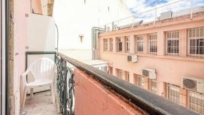A balcony with a white plastic chair, a pink building with multiple windows, and an air conditioning unit. - Happy@chiadosuites12 (Lisboa)