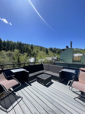 A wooden deck with outdoor furniture, a metal railing, and a view of a forested hillside. - Park City Daly Mountain Dream Free Ski Waxes | Hot Tub | Apres | 2-min Walk to Main (Park City)
