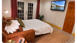 A bedroom with a bed, a TV mounted on the wall, a door, and a window with curtains.