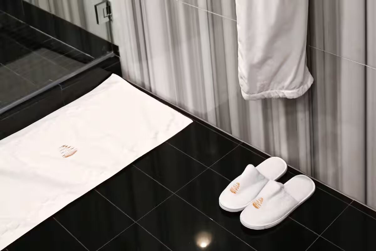 Une salle de bain avec un sol carrelé de carreaux noirs, une serviette blanche accrochée au mur et une paire de chaussons blancs posés sur le sol.