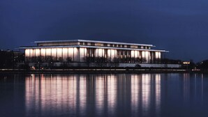 A large, modern building with a long, rectangular structure, reflecting on a calm body of water. - The Watergate Hotel | 2 Superior Rooms | Historic Charm Meets Relaxation (Washington)
