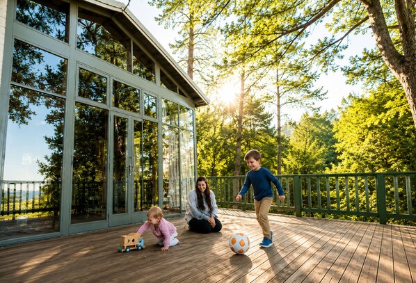 A wooden deck with a glass enclosure, surrounded by trees and a view of the landscape. - Boutique Blue Mountains Cottage | Fireplace • Walk to Town • Relax & Unwind (Katoomba)