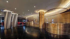 Um lobby moderno de hotel com um balcão de recepção curvo, colunas cilíndricas altas e um piso elegante e refletor.