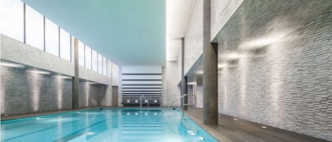 An indoor swimming pool with clear water, surrounded by walls with a textured pattern, and a ceiling with a linear design.
