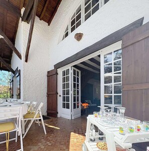 Eine überdachte Terrasse mit Tischen und Stühlen, einem Essbereich und einer großen Schiebetür zu einem Innenraum.