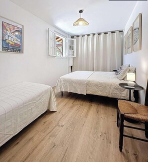 Ein Schlafzimmer mit zwei Betten, einem Fenster mit Vorhängen, einer hängenden Deckenleuchte und einem kleinen Tisch mit einer Lampe.