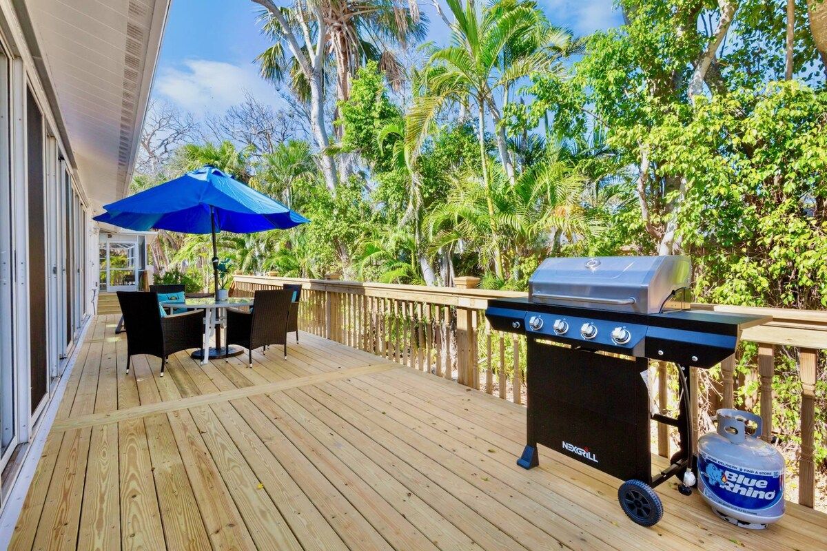 Une terrasse en bois avec un barbecue, du mobilier d’extérieur et un parasol bleu.