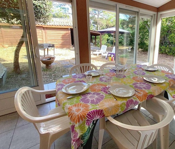 Een eethoek met een tafel voor vier personen, omringd door stoelen, in een kamer met grote ramen en uitzicht op de achtertuin.