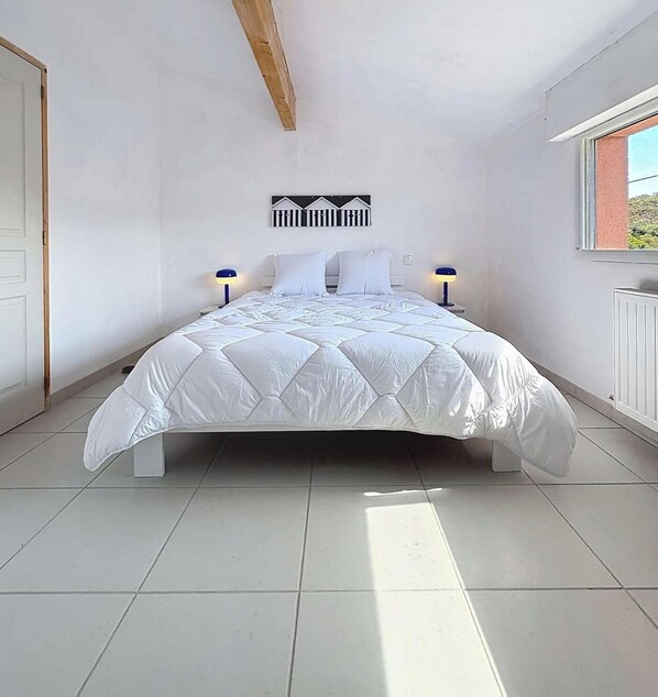 Ein Schlafzimmer mit einem Bett, zwei Nachttischlampen, einem Deckenbalken und einem Fenster.