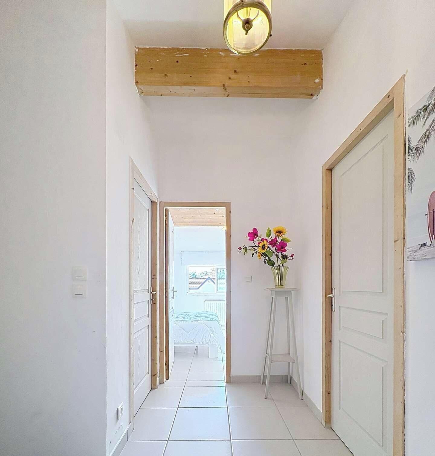 Ein Korridor mit weißen Wänden, einem Fliesenboden, einem Holzbalken an der Decke und einer Tür rechts.