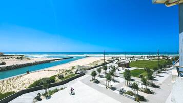 Vista costera con playa, río y paseo marítimo con bancos y árboles.