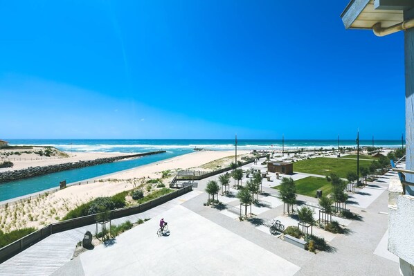Vista costera con playa, río y paseo marítimo con bancos y árboles.