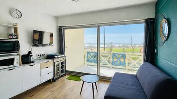Un espacio habitable compacto con kitchenette, un sofá, una mesita y un balcón con vistas.