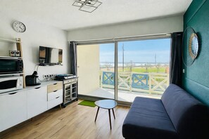 Un espacio habitable compacto con kitchenette, un sofá, una mesita y un balcón con vistas.