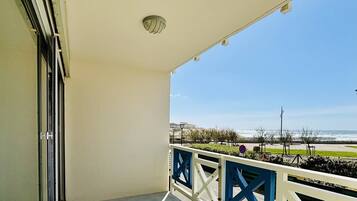 Un balcón con vista al mar, barandilla blanca y una puerta a la izquierda.