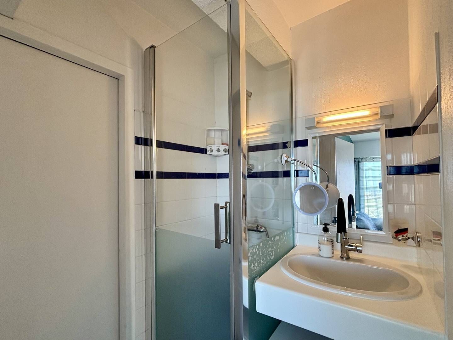 Un baño con cabina de ducha de vidrio, un lavabo blanco y un espejo.